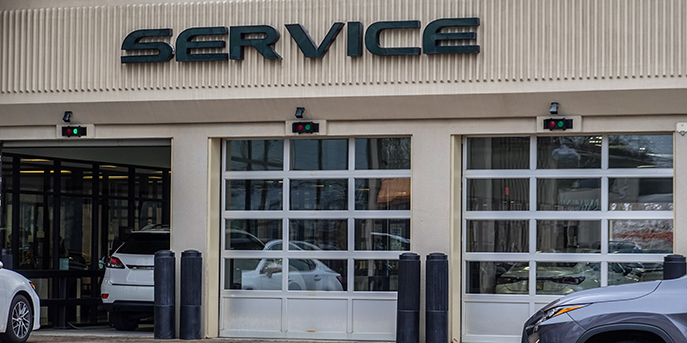 Three bays in an auto service center. One bay is open and accepting new cars, indicated by the lit green light; the other two are closed. 