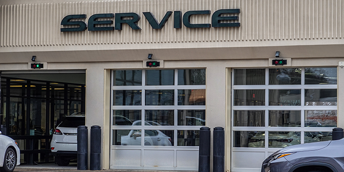 Three bays in an auto service center. One bay is open and accepting new cars, indicated by the lit green light; the other two are closed.