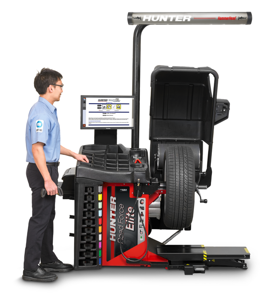 A technician stands next to Hunter's Road Force® Elite wheel balancer. There is a tire in the wheel balancer.