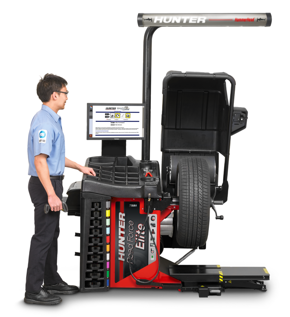 A technician stands next to Hunter's Road Force® Elite wheel balancer. There is a tire in the wheel balancer.