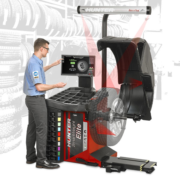 A technician is operating a computer connected to Hunter's SmartWeight® Elite wheel balancer. the wheel balancer is open, no tire has been mounted yet.