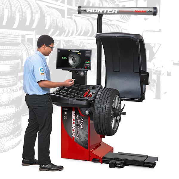 A technician stands at a computer connected to the Hunter SmartWeight Pro. A tire has been mounted onto the machine.