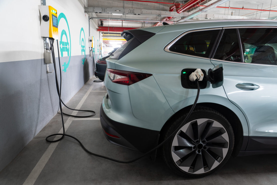 A blue electric vehicle van is being charged at a charging station inside of a bay