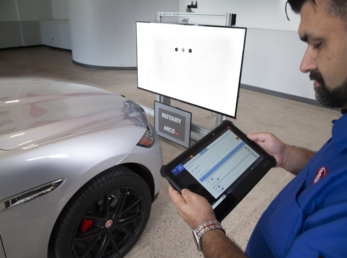 A tech looks at a tablet. There is a frame in the background with a calibration target on it.