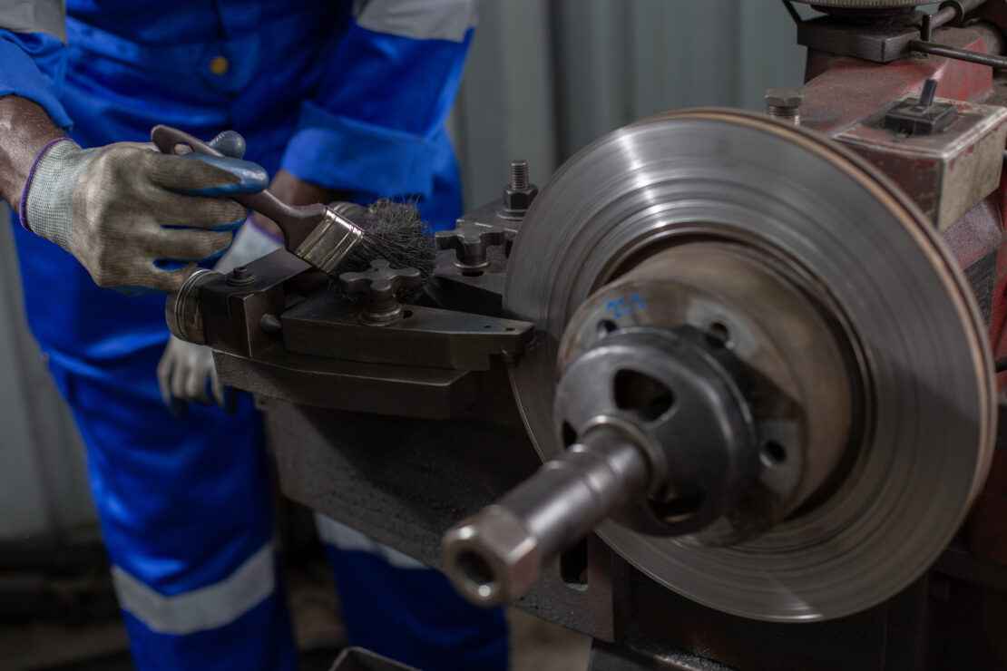 A technician uses a brush to clean off a dirty brake lathe.